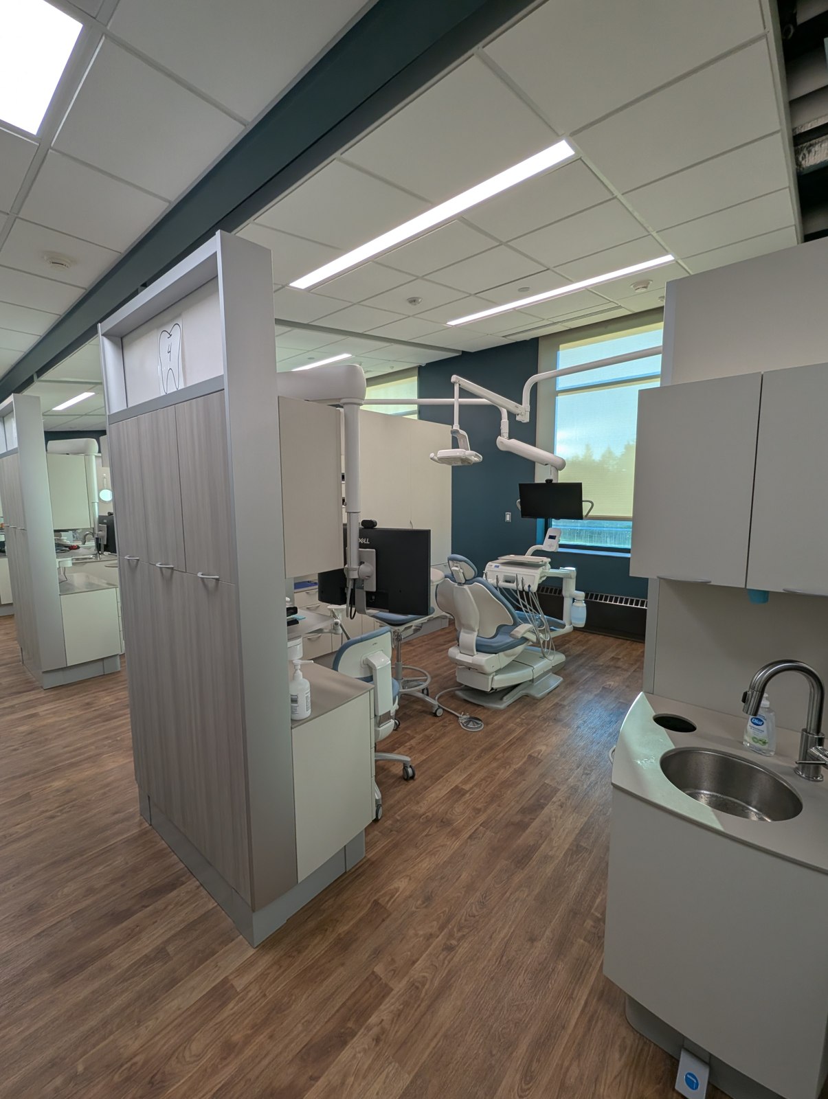 Dental treatment suite with clinical equipment, ceiling lights, and wood-look flooring